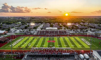 aerial view of football field with sunset over town in back