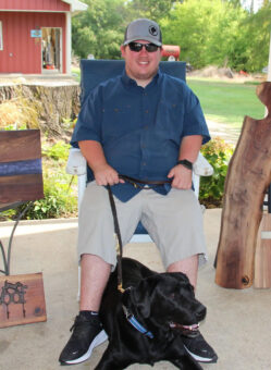 Josh Hass sitting in chair outside holding leash with black lab