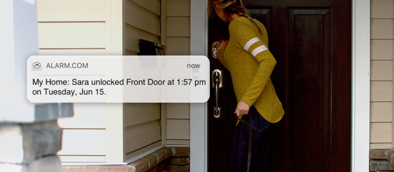 woman at door with alarm.com message showing "My Home: Sara unlocked Front Door at 1:57 p.m. on Tuesday, June 15."