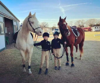 2 young kids next to 2 horses